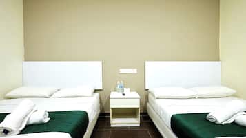 Habitación de hotel con dos camas, cada una con ropa blanca y colchas verdes. Se observa una mesita de noche pequeña con un control remoto, una botella de agua y una caja de pañuelos.