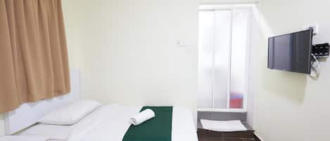 A hotel room with a bed, a TV mounted on the wall, an air conditioning unit, and a window with curtains.