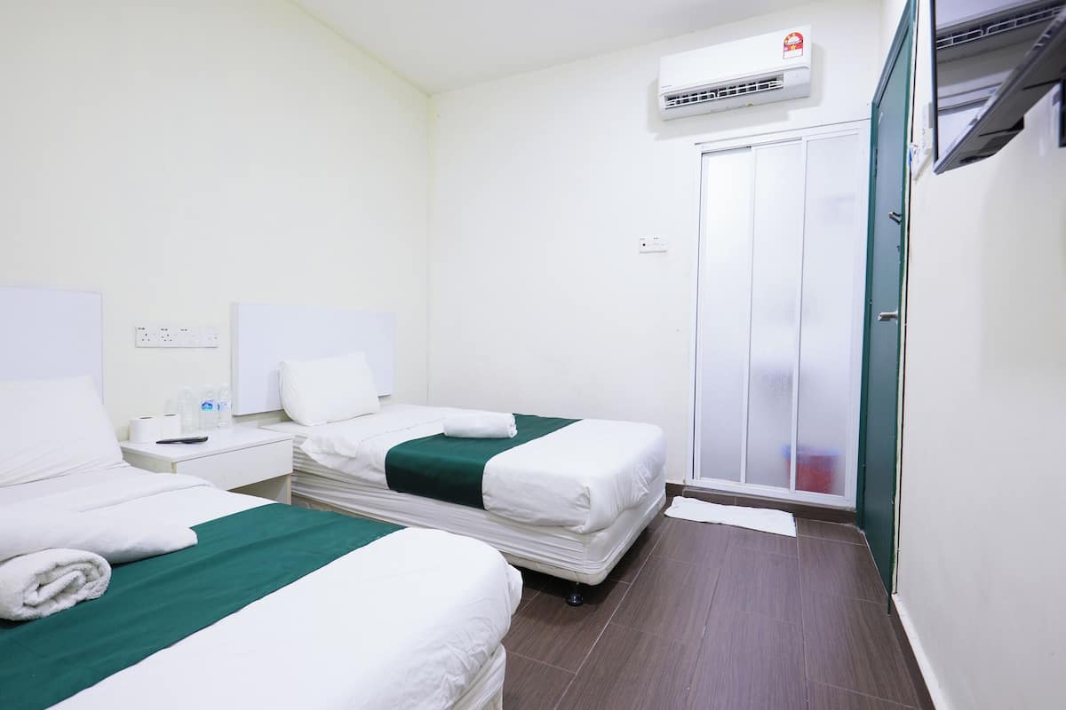 Habitació d'hotel amb dos llits, un armari, un aire acondicionador i una taula petita amb un comandament a distància.
