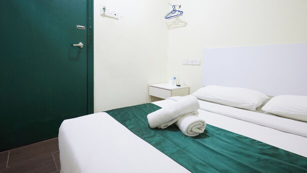 A hotel room with a green bedspread, white pillows, a neatly made bed, a small bedside table with a lamp, and a green door. - Fast Hotel Sri Gombak By Zuzu (Batu Caves)