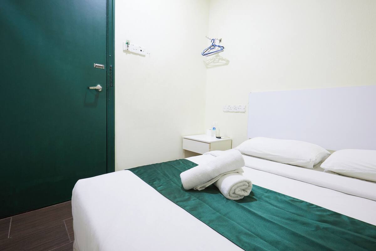 Habitació d'hotel amb un llit, estriat verd, almoines blanques, una nit de nit amb una làmpada i una perxa blava a la paret.