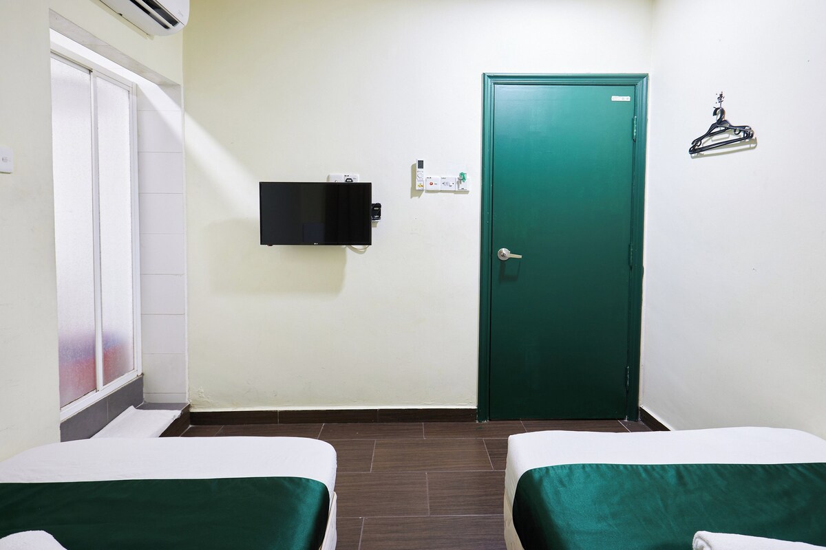 Una habitación con dos camas, una puerta verde, un televisor montado en la pared y un perchero.
