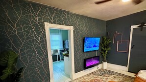 Un dormitorio con cama, televisor, planta pequeña y puerta que da a un baño.