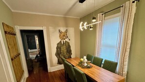 Comedor con mesa de madera, sillas tapizadas en verde, lámpara de pared y un mural decorativo con un zorro.