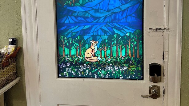 Una puerta con un vitral que muestra una estrella, un zorro y una escena de bosque.