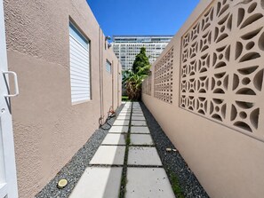 A narrow pathway flanked by beige walls with decorative cutouts, leading to a building with a white facade and windows.