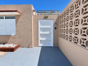 A building entrance with a beige wall, a white door with a mesh screen, and a numbered sign.