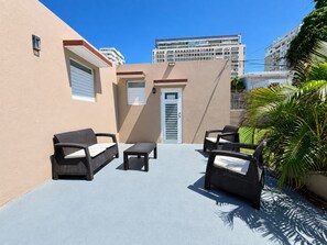An outdoor patio with wicker furniture, a door, and a building in the background.