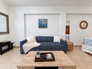 A living room with a blue sofa, a coffee table with remote controls, and a painting on the wall.