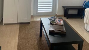 A room with a white wardrobe, a door with blinds, a black table with a magazine, a blue chair, and a mirror on the wall.