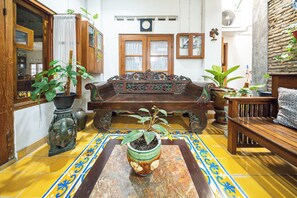 Una habitación tradicional con un sofá de madera, una mesita con una planta en maceta y un suelo de baldosas con un borde decorativo.