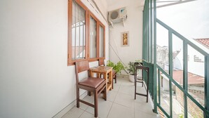 A balcony with wooden furniture, a potted plant, and a view of buildings. - Omah Gerjen 29 By Zuzu (Yogyakarta)