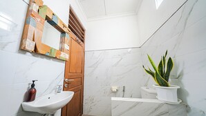 Un baño con lavamanos, espejo, puerta de madera, baldosas de mármol, una planta en maceta y un inodoro.