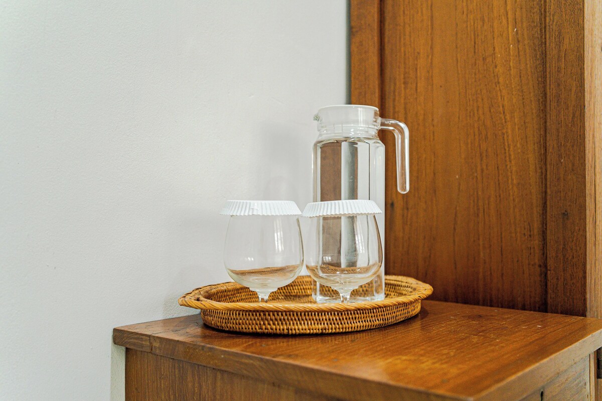 A clear glass pitcher and two glasses on a wooden surface with a wicker tray.