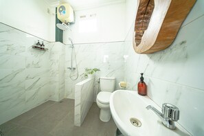 A bathroom with a toilet, sink, shower, and marble tiles. - Omah Gerjen 29 By Zuzu (Yogyakarta)