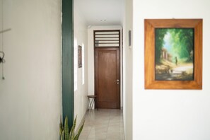 A hallway with a wooden door, a small stool, a framed painting, and a potted plant. - Omah Gerjen 29 By Zuzu (Yogyakarta)