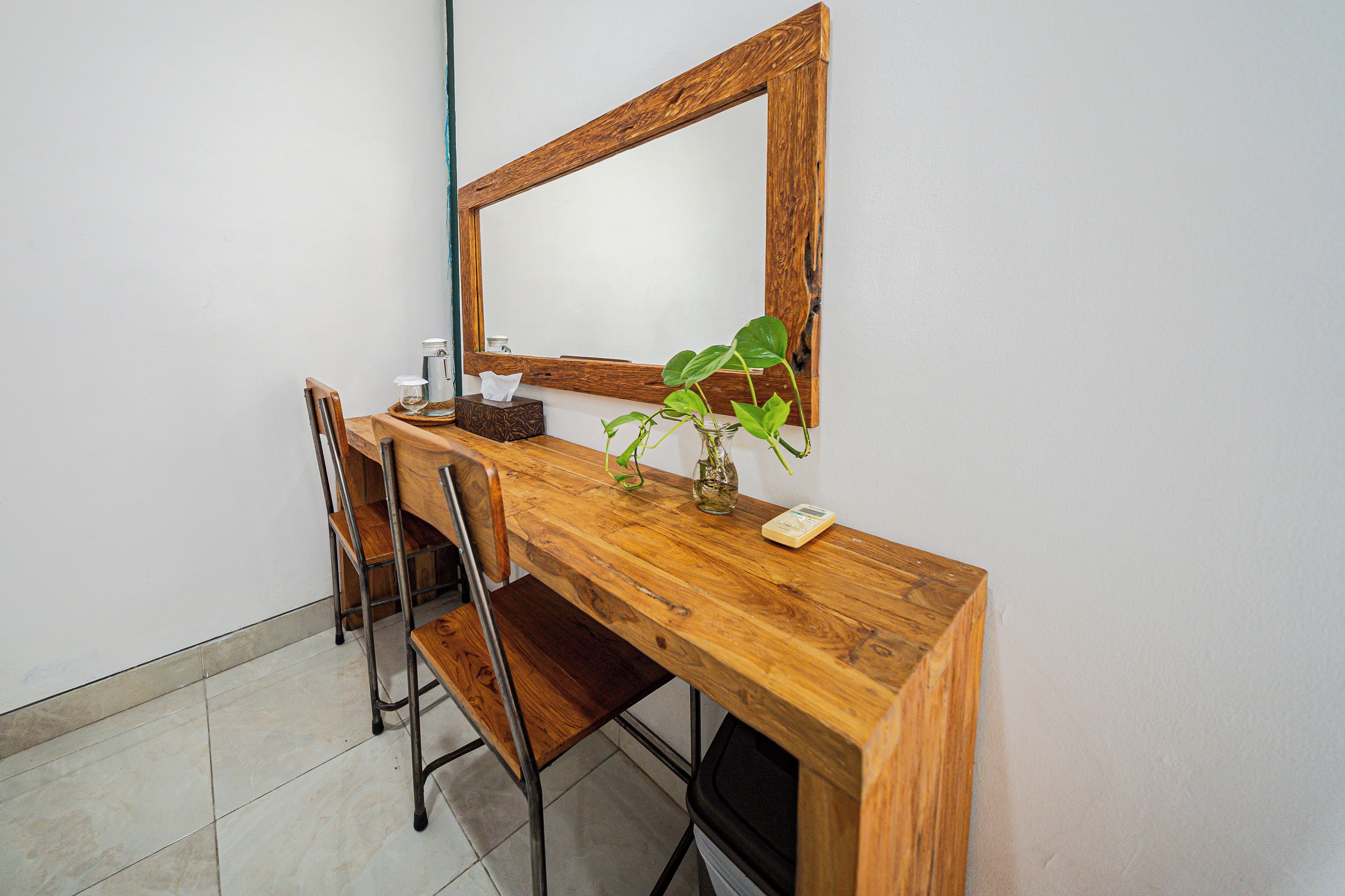 A wooden desk with a mirror, a chair, a plant, and a tissue box.