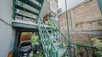 A narrow alleyway with a green metal staircase leading to a second-floor apartment. There are potted plants and a parked car visible.
