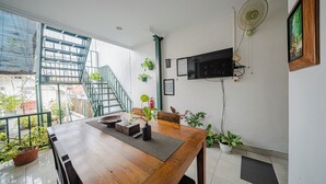 A dining area with a wooden table, potted plants, a staircase, and a mounted television. - Omah Gerjen 29 By Zuzu (Yogyakarta)