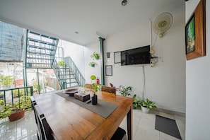 A dining area with a wooden table, potted plants, a staircase, and a mounted television. - Omah Gerjen 29 By Zuzu (Yogyakarta)