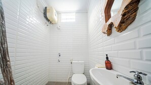 A bathroom with white tiled walls, a white toilet, a sink with a faucet, and a soap dispenser. - Omah Gerjen 29 By Zuzu (Yogyakarta)