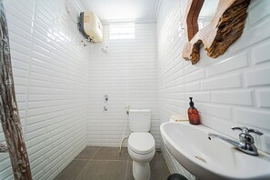 Un baño con paredes de azulejos blancos, un inodoro blanco, un lavamanos con grifo y dispensador de jabón.
