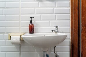 Un baño con lavamanos blanco, dispensador de jabón y soporte para papel higiénico.