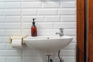 Un baño con lavamanos blanco, dispensador de jabón y soporte para papel higiénico.