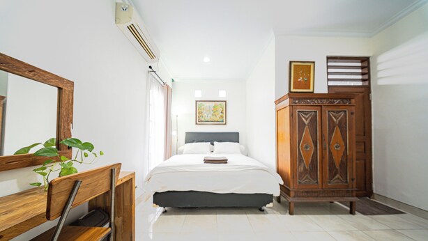 A bedroom with a bed, a wooden wardrobe, a mirror, and a plant. - Omah Gerjen 29 By Zuzu (Yogyakarta)