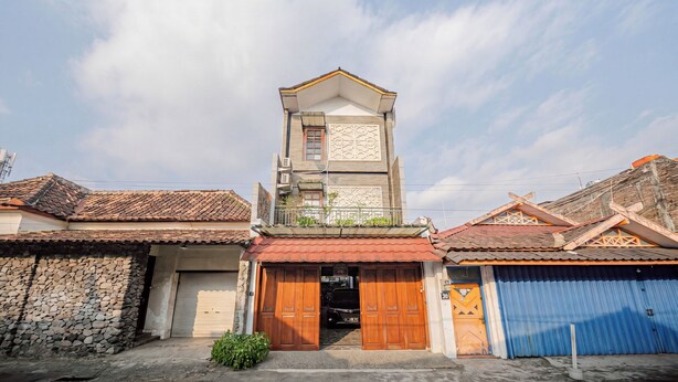Un edificio a due piani con un ingresso centrale, un balcone e un muro in pietra sulla sinistra.