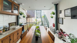 A kitchen with wooden cabinets, a dining table with a plant centerpiece, and a staircase leading to an upper level. - Omah Gerjen 29 By Zuzu (Yogyakarta)