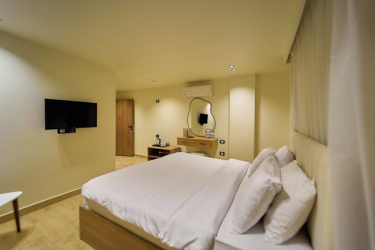 A hotel room with a bed, a TV mounted on the wall, a bedside table, and a mirror.