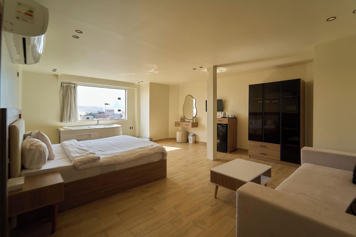 Habitación de hotel con cama, sofá, escritorio, armario, espejo y ventana con vistas.