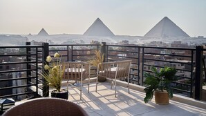 A balcony with a view of the pyramids, wicker chairs, and potted plants. - Merak Pyramids View Hotel (Giza)