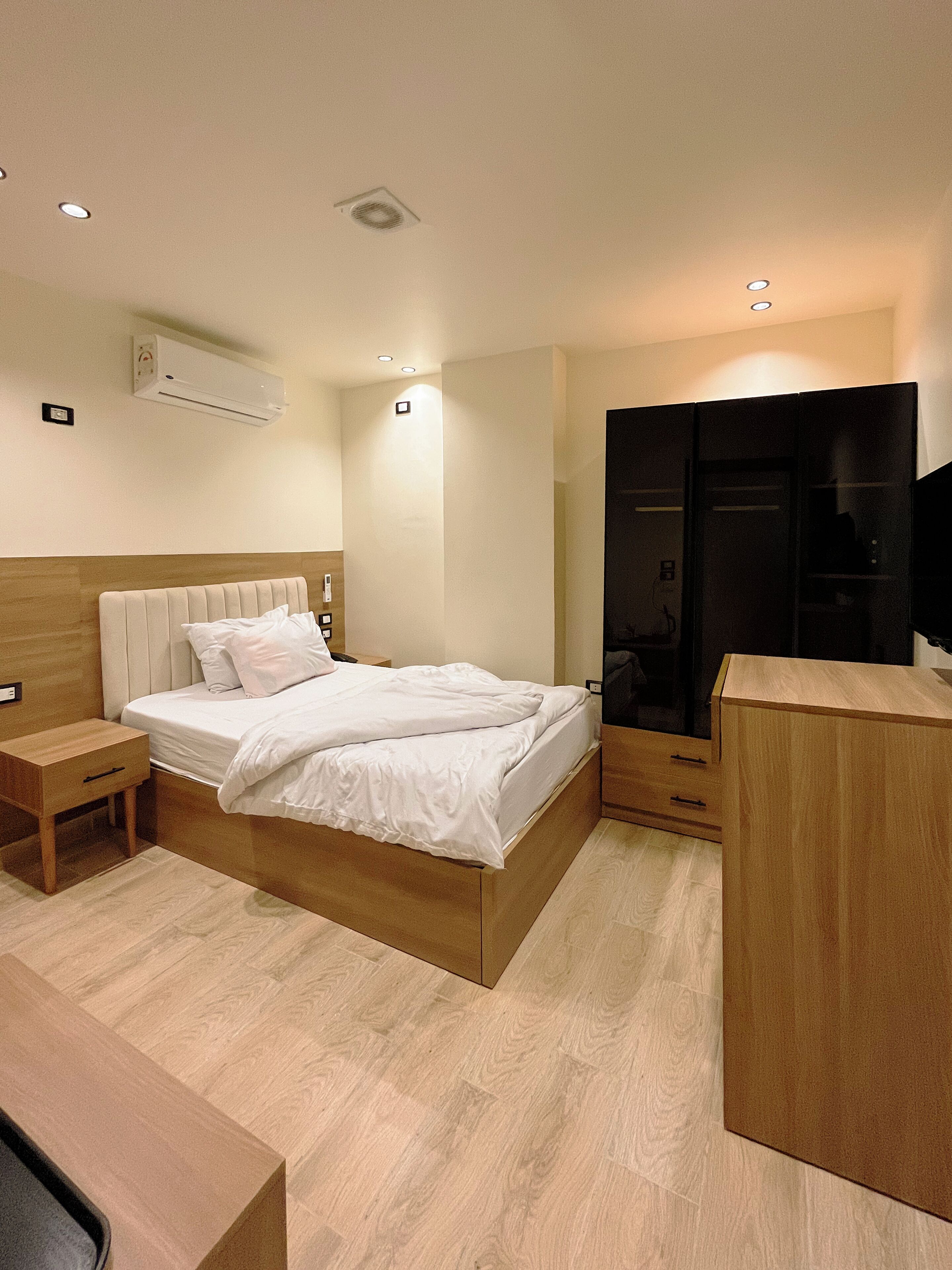 Ein modernes Schlafzimmer mit einem hölzernen Bett, Nachttischen, einem Kleiderschrank und einer Klimaanlage.
