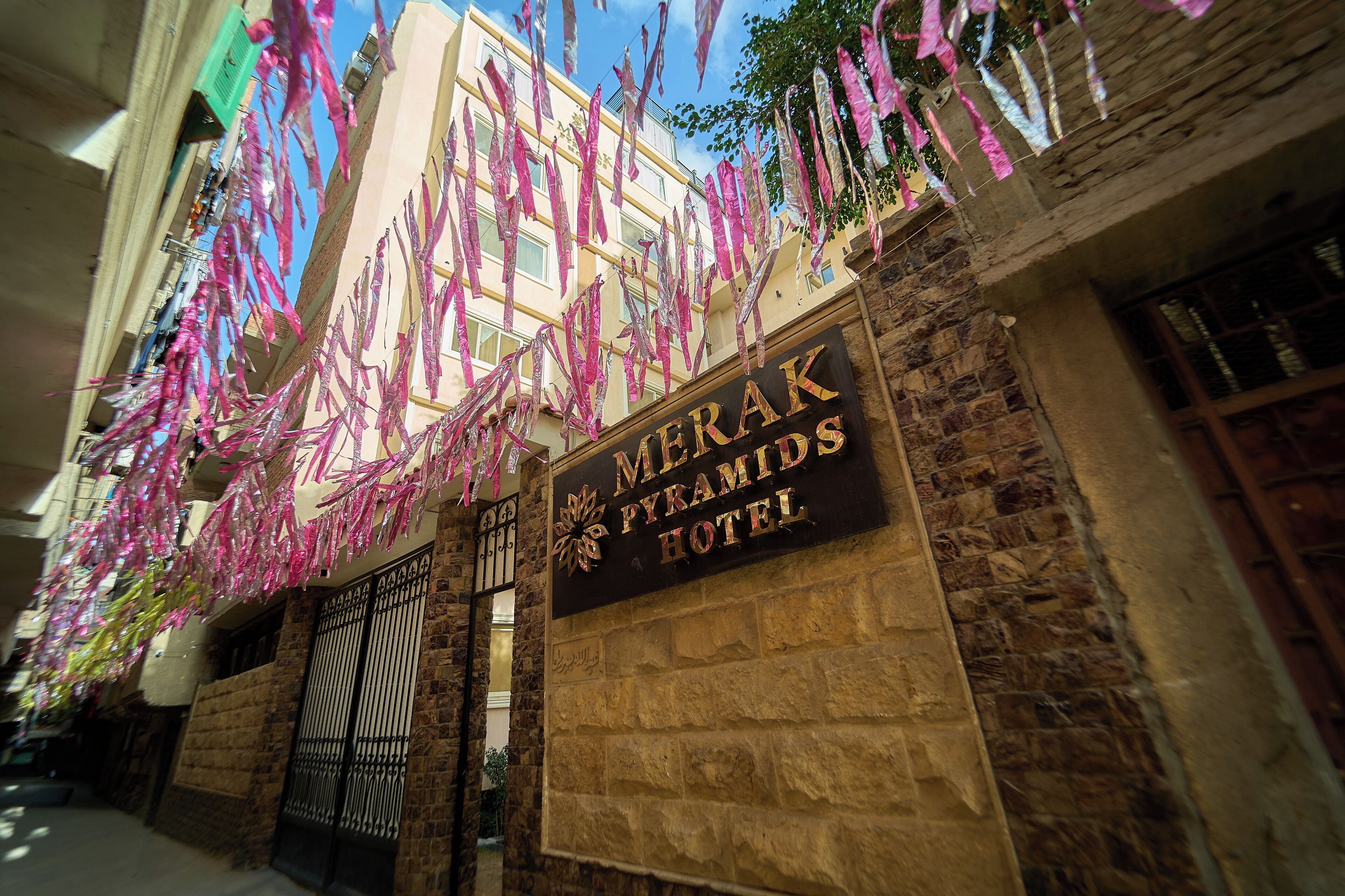 The exterior of the Merak Pyramids Hotel with stone walls and a signboard.