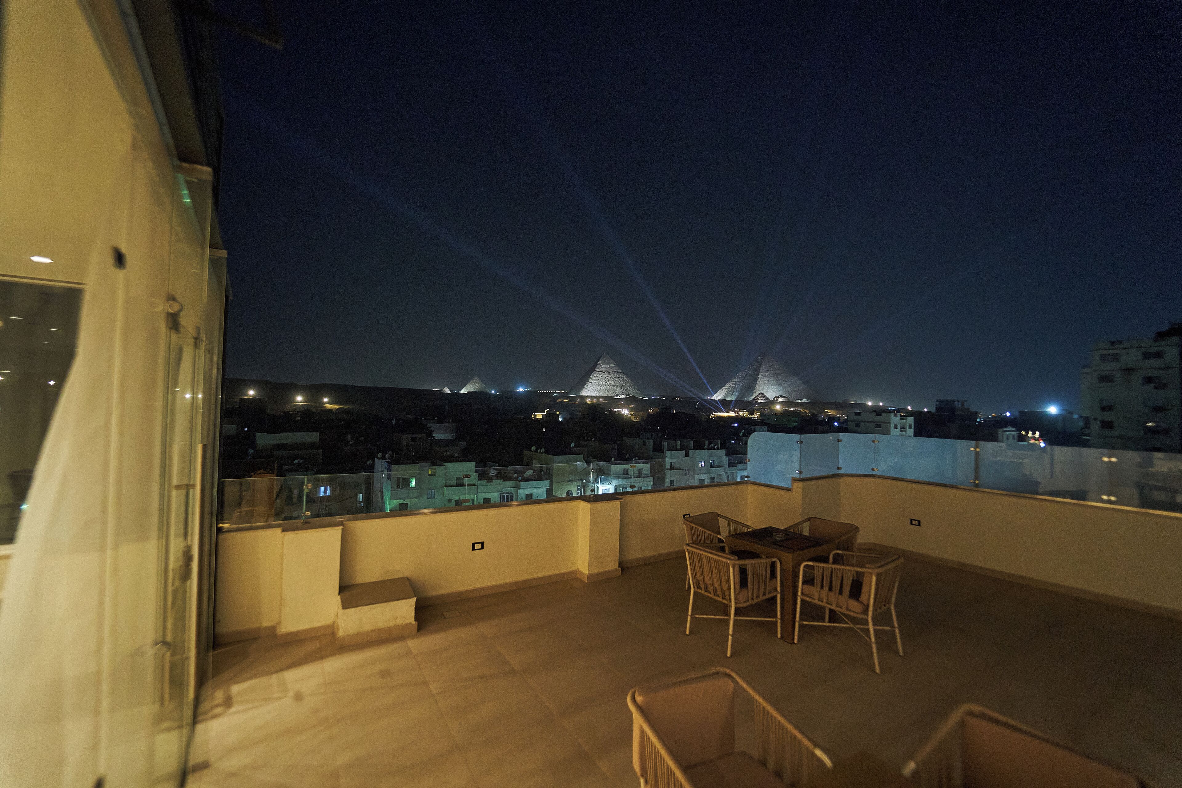 En takterrass med utsikt över en pyramidformad byggnad och den omgivande stadsbilden i nattljus.