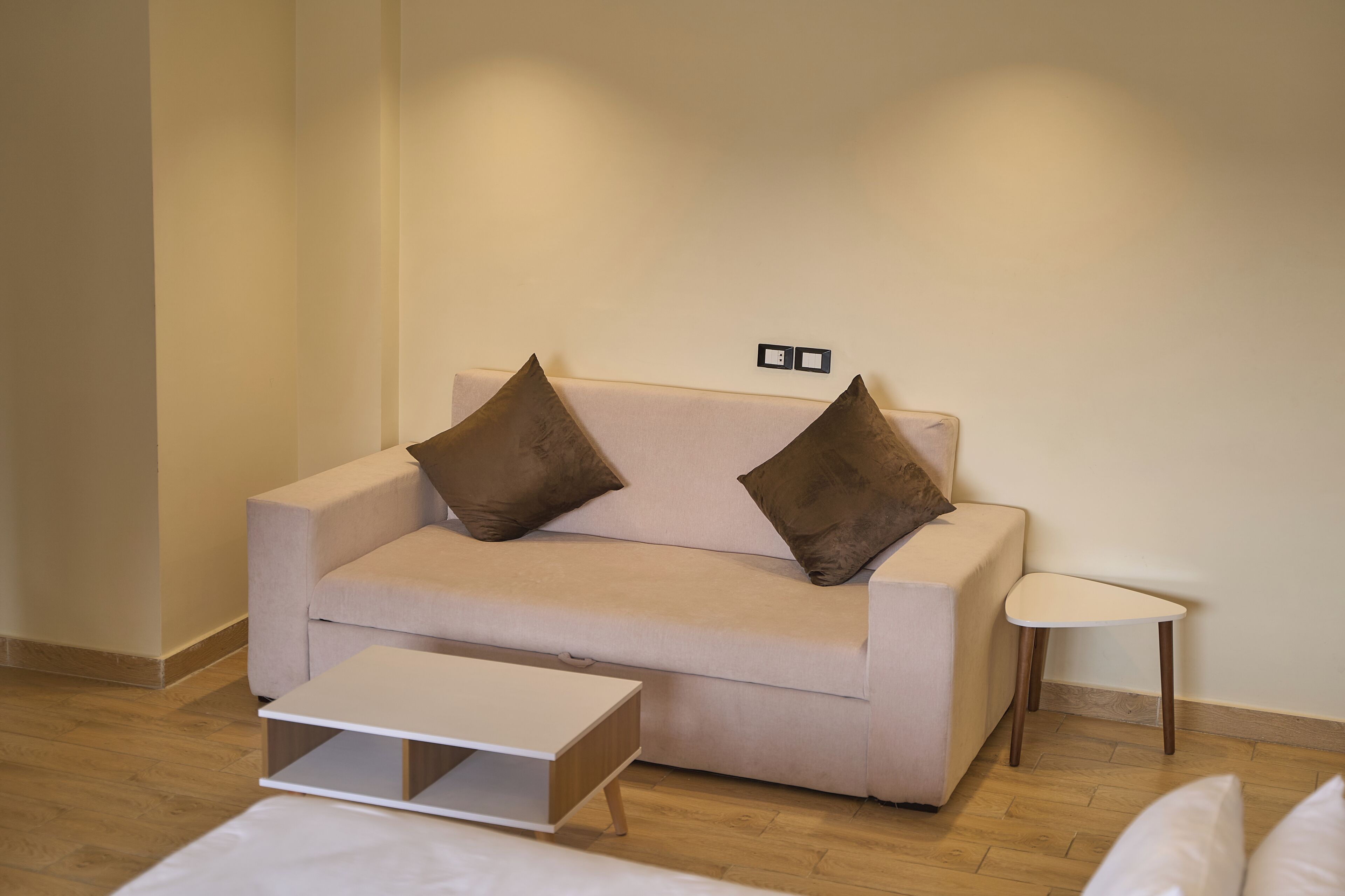A neutral-colored sofa with two pillows, a small white side table, and a wooden floor.