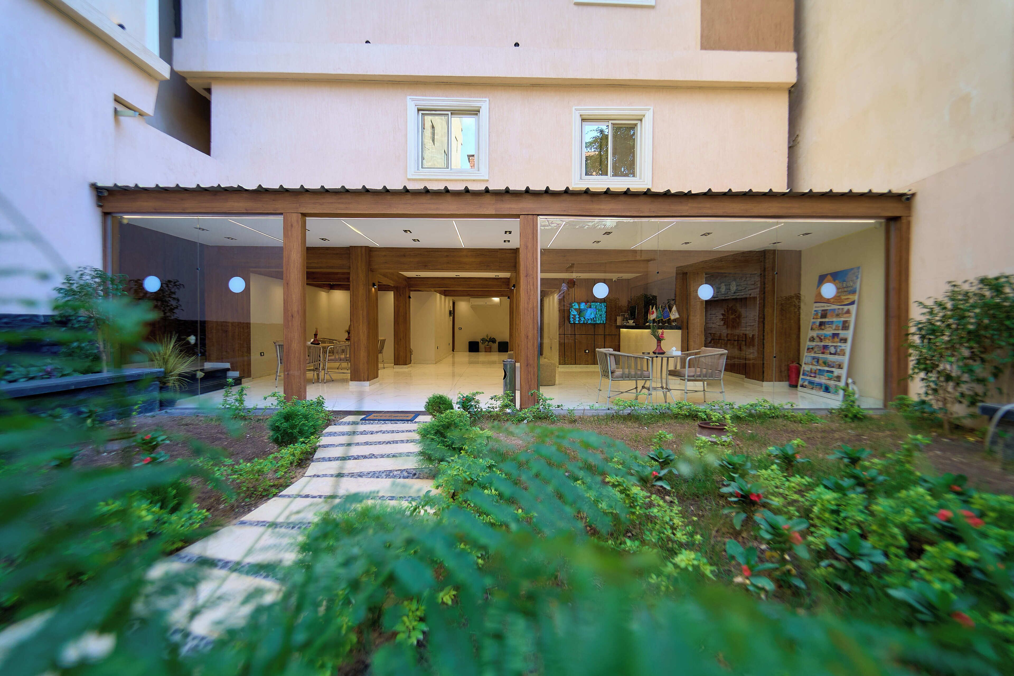 Un edificio moderno con un porche cubierto, un jardín con un sendero y una zona de estar con mesas y sillas.