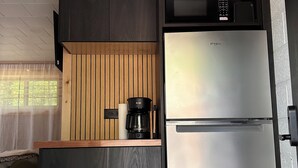 Een kleine keuken met donker houten kastjes, een roestvrijstalen koelkast en een koffiezetapparaat op het aanrecht.