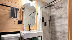 Een badkamer met een houten wand, een witte wastafel, een spiegel, een toilet en een douchehoek.