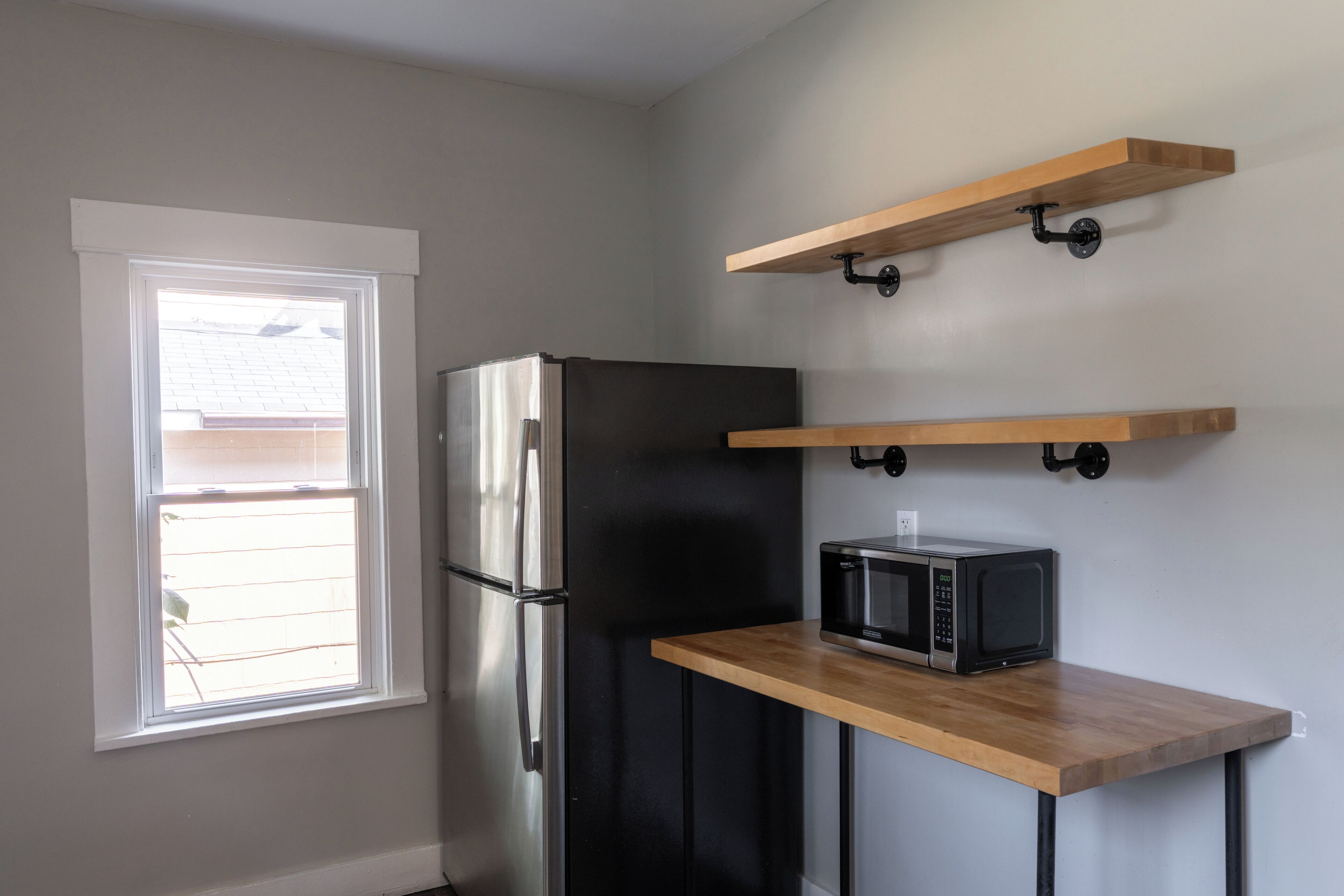 A kitchen with a refrigerator, microwave, and wooden shelves.