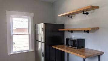 A kitchen with a refrigerator, microwave, and wooden shelves.