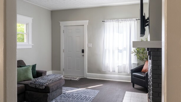 Ein Wohnzimmer mit grauem Sofa, schwarzem Sessel, weißer Tür und Kamin.