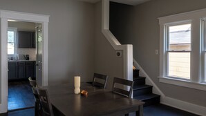 Ein Essbereich mit einem dunklen Holztisch, zwei Stühlen, einer Kerze und einer kleinen Schüssel. Eine Treppe führt zu einer zweiten Etage.
