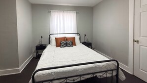 Ein Schlafzimmer mit einem Einzelbett, zwei Nachttischen, einem Schrank und einem Fenster mit weißen Vorhängen.
