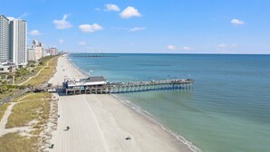 Une plage avec une jetée qui s’avance dans l’océan, bordée d’un paysage urbain avec de hauts immeubles.
