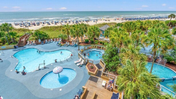 Een resort met meerdere zwembaden, een strandgedeelte en palmbomen.