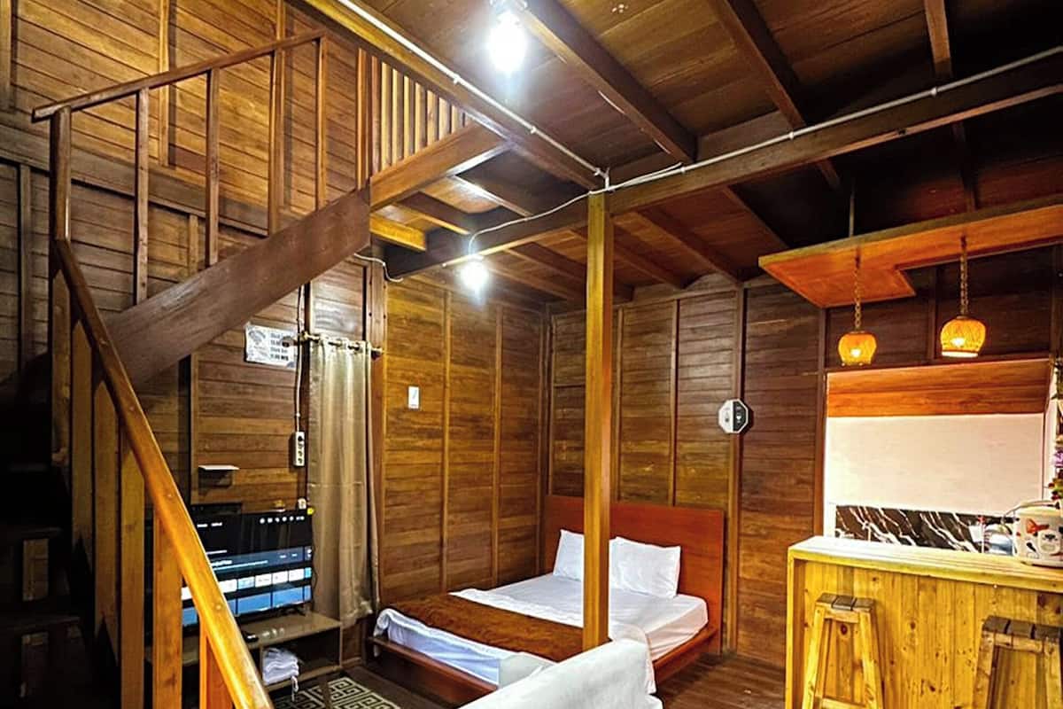 A wooden cabin interior with a staircase, a bed, a desk, and a bar area.