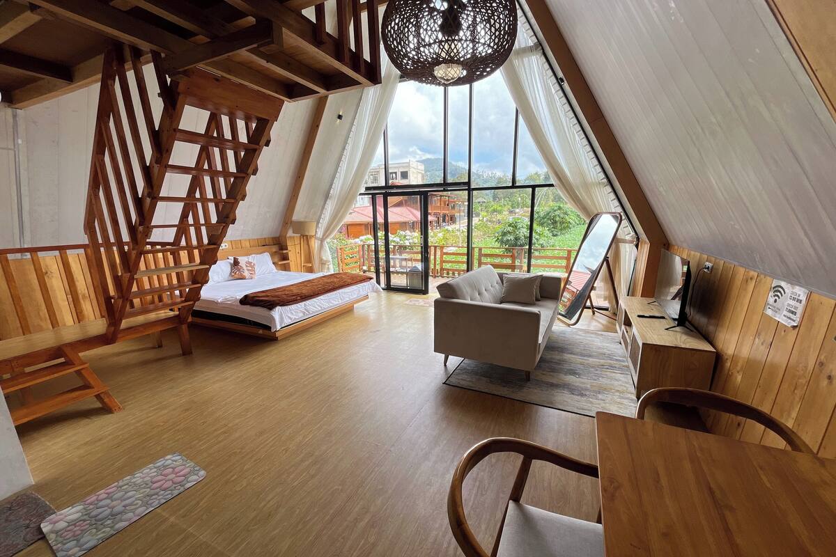 A cozy room with a wooden staircase, a bed, a sofa, and a desk with a chair.